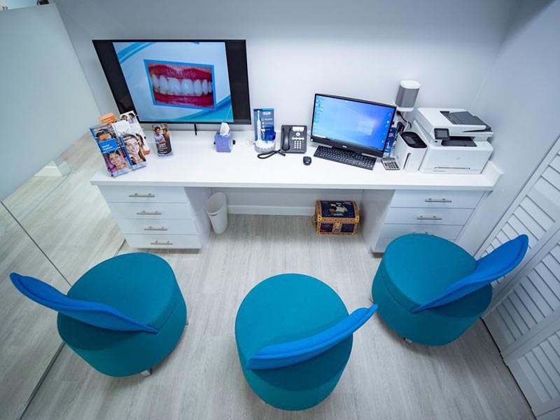 A modern dental office with a reception area featuring a desk, computer monitor, and various seating options.