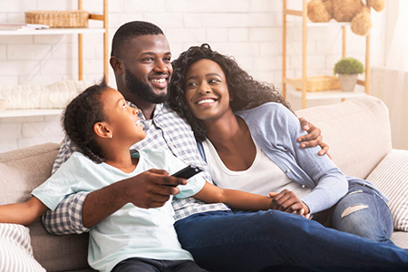 A family of four sitting on a couch, with two adults and two children, all smiling and looking at something off-camera.
