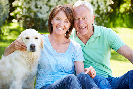 A man and woman are sitting on grass with a golden retriever between them  they all appear happy and relaxed, likely enjoying a sunny day outdoors.