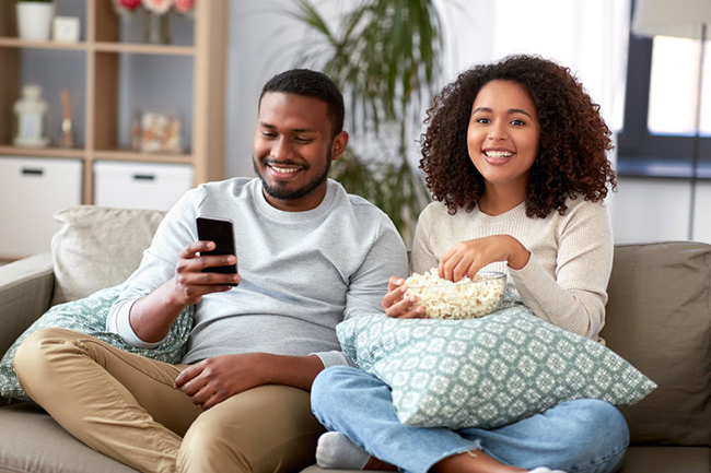 A man and woman are sitting on a couch, sharing a moment together while watching something on their phones.
