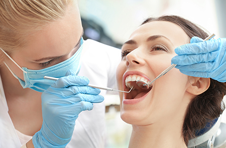 In the image, a dental hygienist is performing a teeth cleaning procedure on a patient using specialized tools while wearing protective gloves and a face mask.